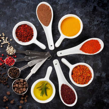Padstal Deli premium gourmet condiments and spices collection feature, showcasing an assortment of colorful culinary spices, herbs, and oils arranged in white tasting spoons on a dark slate background.