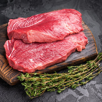 Padstal Deli premium wild game meat collection feature, displaying two raw venison steaks (wildsvleis) on a dark wooden cutting board with fresh herbs.