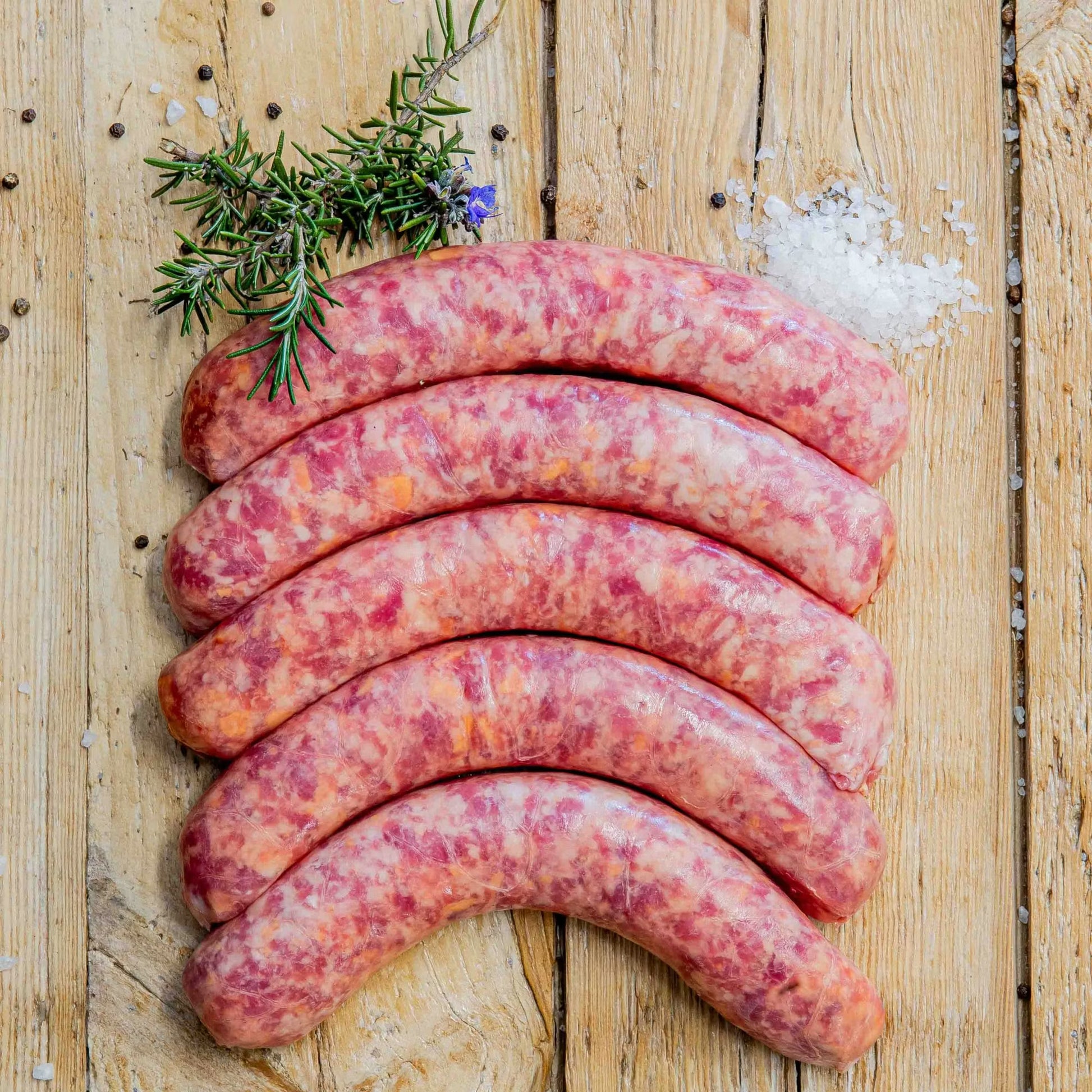 Padstal Deli premium raw Gerookte Kaaswors (Smoked Cheese Grillers) arranged on a light rustic wooden background, decorated with coarse sea salt, black peppercorns, and fresh rosemary.