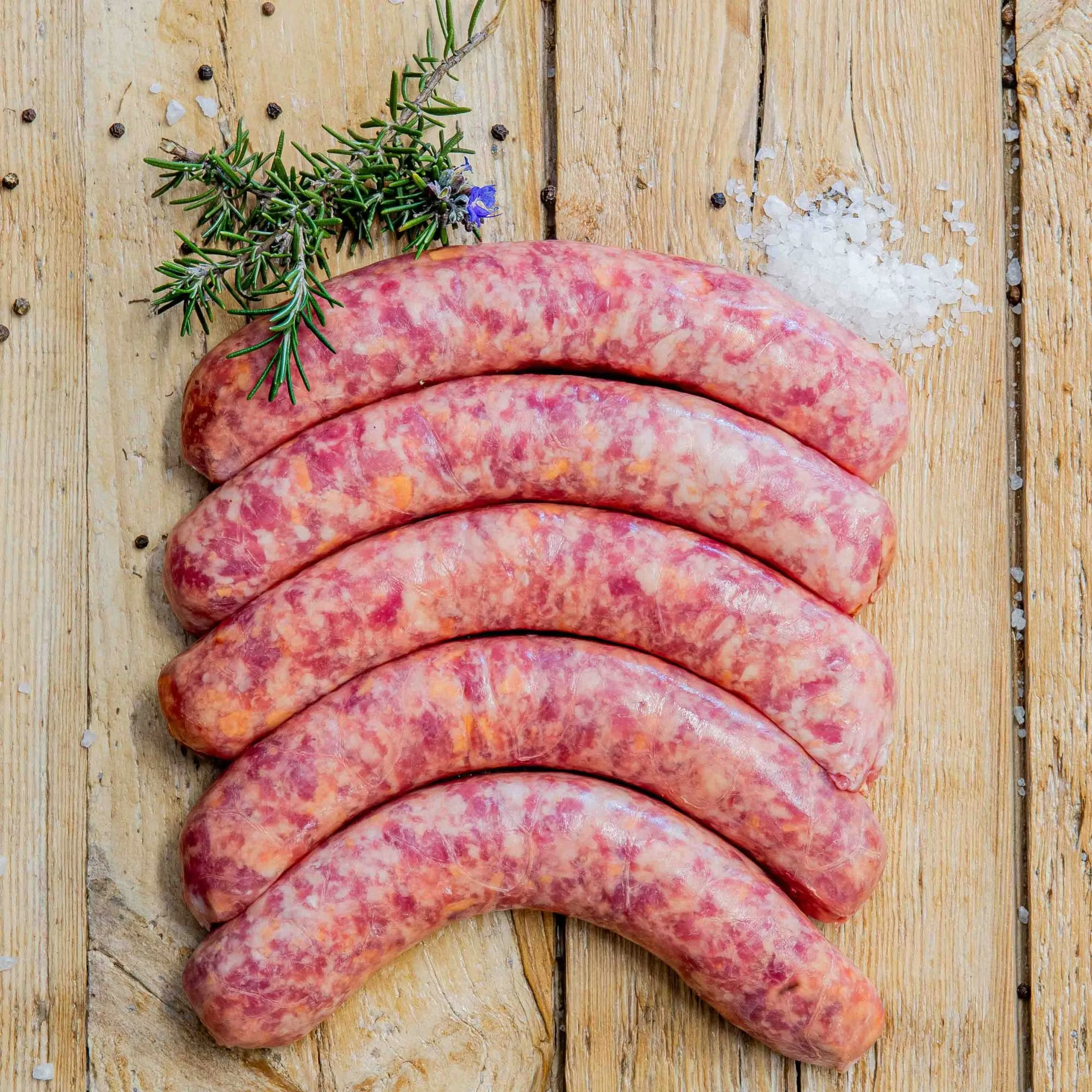 Padstal Deli premium raw Gerookte Kaaswors (Smoked Cheese Grillers) arranged on a light rustic wooden background, decorated with coarse sea salt, black peppercorns, and fresh rosemary.
