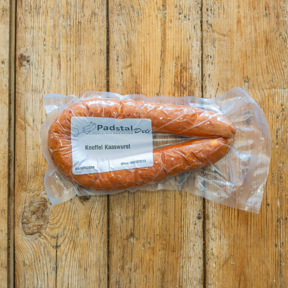 Image showing a Padstal Deli branded Knoffel Kaaswurst in vacuum-packed packaging, laying on a vertical grained light wooden backdrop