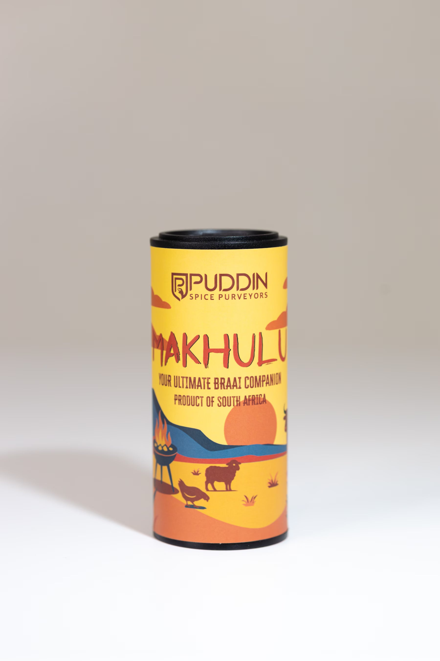 A cylindrical metal tin of Puddin Spice Purveyors Makhulu, featuring a yellow and orange illustrated label with a sunset landscape and animal silhouettes, set against a neutral light gray background.