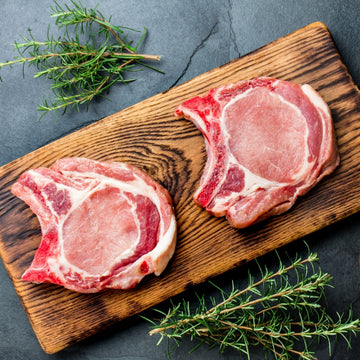 Padstal Deli premium pork collection feature, displaying two raw bone-in pork chops on a rustic wooden cutting board styled with fresh rosemary sprigs.