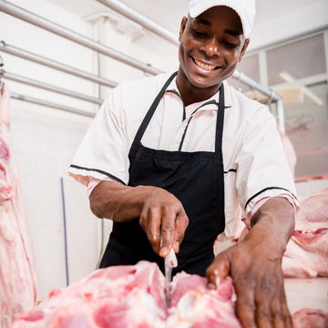 A smiling Padstal Deli butcher expertly cutting premium raw meat at a professional meat processing facility.