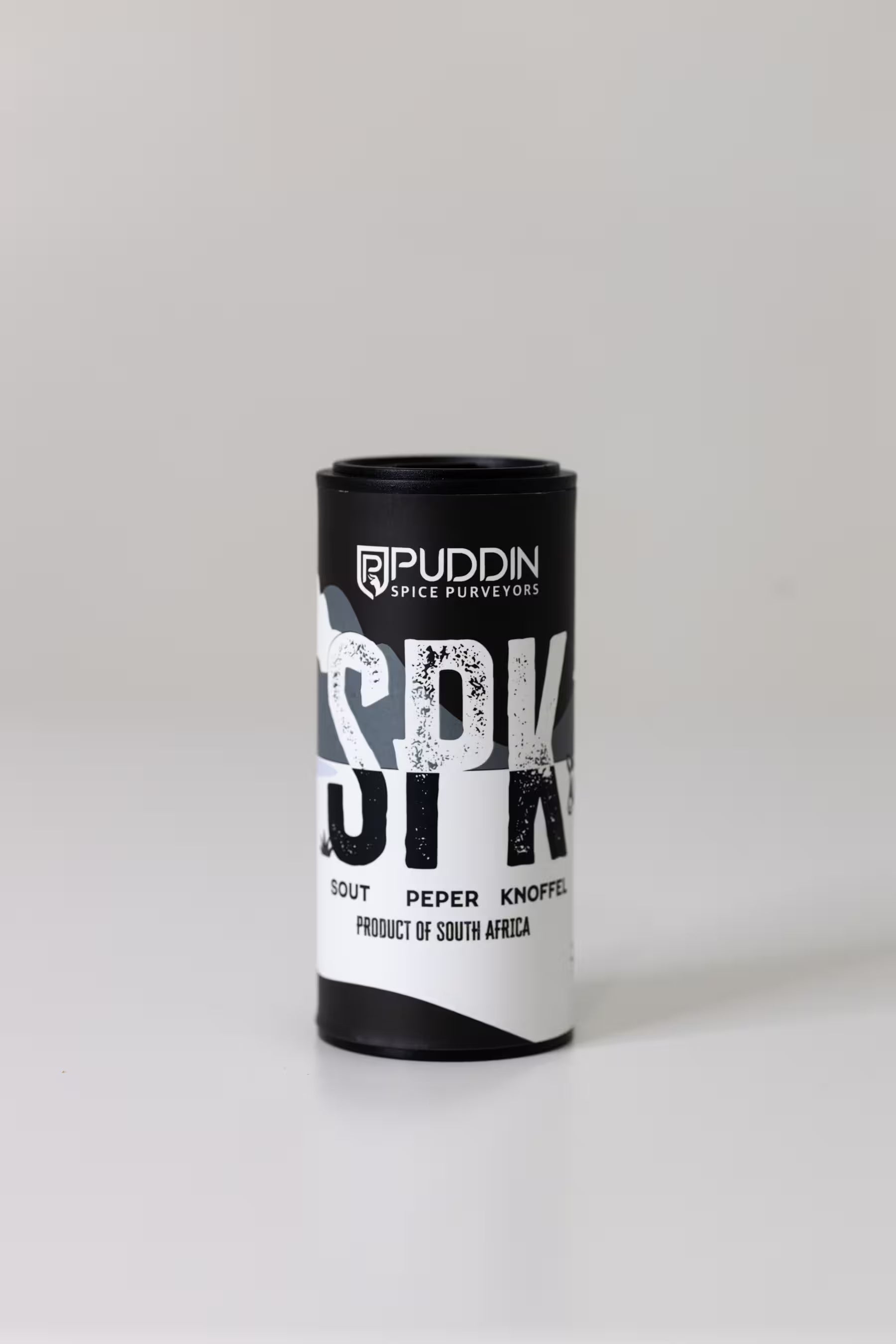 A black and white cylindrical tin of Puddin Spice Purveyors 'SPK' (sout peper knoffel) standing upright on a light gray background.