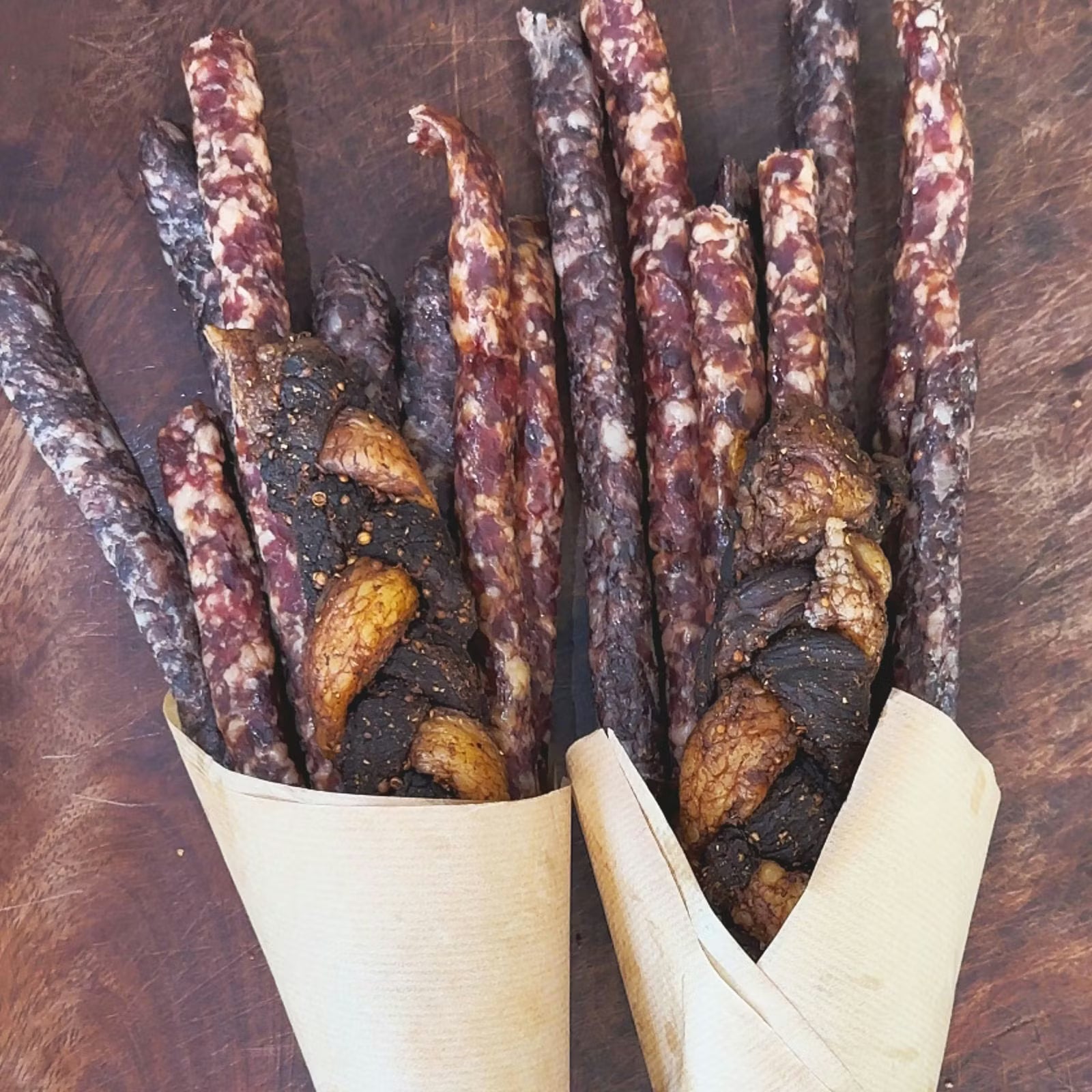 Two Padstal Deli Baby Biltong Bouquets wrapped in light brown craft paper, featuring premium dried meat sticks, droëwors, and braided chilli bites arranged on a dark wooden surface.