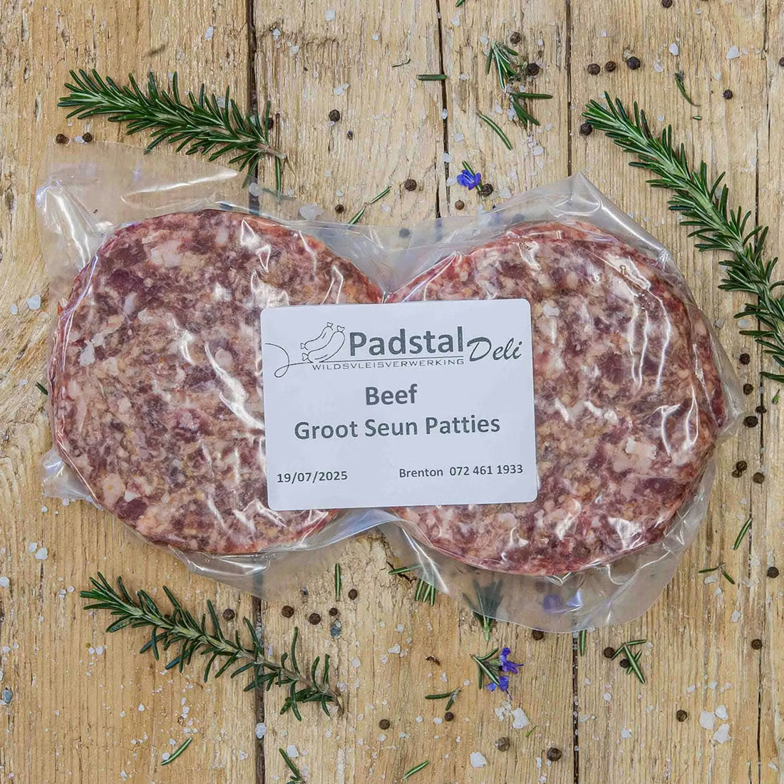 Padstal Deli premium raw burger patties arranged on a rustic wooden background, garnished with dried bay leaves, fresh rosemary sprigs, coarse salt, and peppercorns.