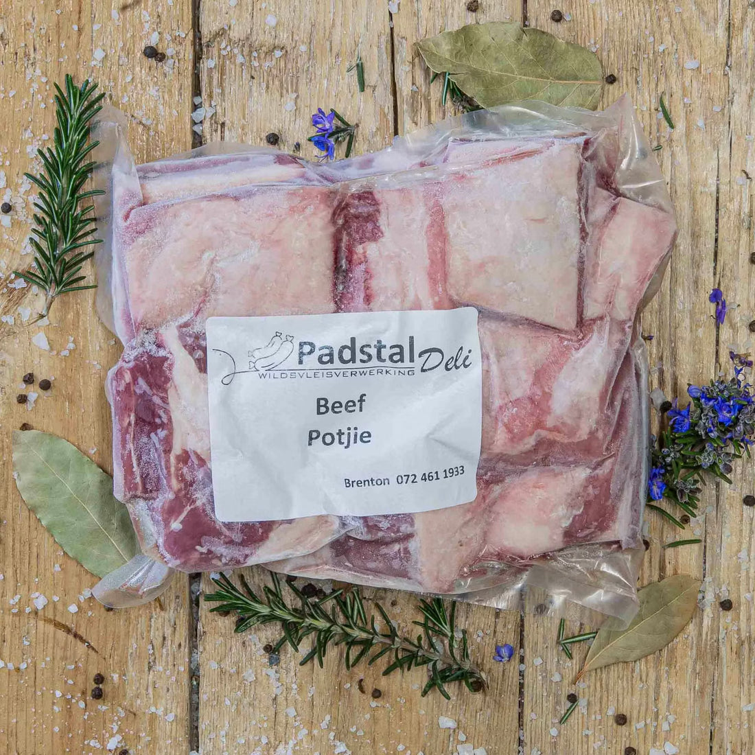Padstal Deli vacuum-sealed premium bone-in Beef Potjie meat cuts resting on a rustic wooden background, decorated with dried bay leaves, fresh rosemary, coarse salt, and peppercorns.