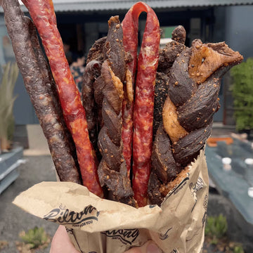 Padstal Deli premium Biltong and Droëwors bouquet gift bag featuring whole beef biltong carvings, traditional braided biltong, and dry snap sticks bundled in a branded brown paper wrapper.