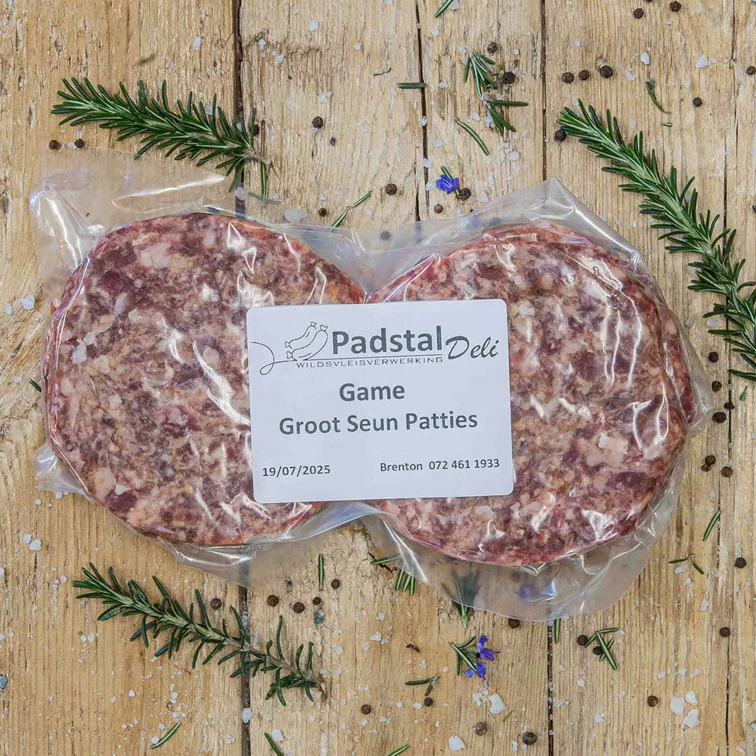 Padstal Deli premium raw burger patties arranged on a rustic wooden background, garnished with dried bay leaves, fresh rosemary sprigs, coarse salt, and peppercorns.
