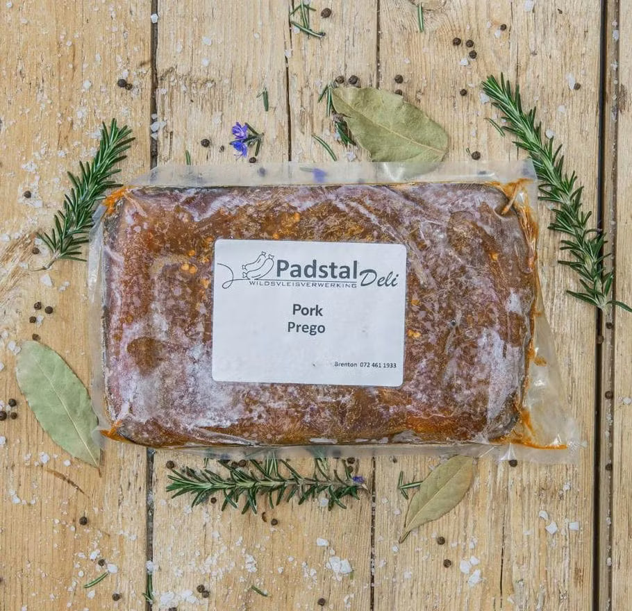 Padstal Deli vacuum-sealed premium marinated Pork Prego meat resting on a rustic wooden background, decorated with dried bay leaves, fresh rosemary, coarse salt, and peppercorns.