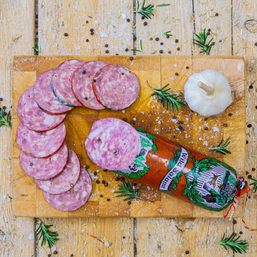 Padstal Deli premium Wild Salami stick with gourmet slices arranged on a wooden cutting board, garnished with a whole garlic bulb, coarse salt, and fresh rosemary.