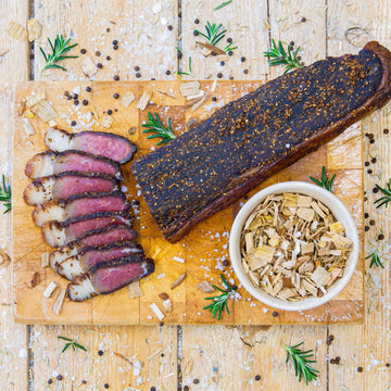 Padstal Deli Smoked Biltong featuring a whole slab alongside gourmet slices with thick yellow fat on a wooden cutting board, garnished with spices and fresh rosemary.